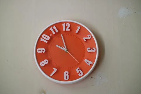 Round orange wall clock with hands indicating 10 am Stock Photos