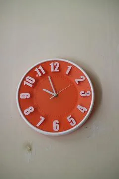 Round orange wall clock with hands indicating 10 am Stock Photos