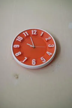 Round orange wall clock with hands indicating 10 am Stock Photos