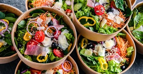 Round paper boxes with pre-packaged vegetable salads ready for sale Stock Photos
