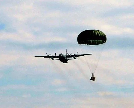 A round parachute carries a cargo load dropped out of a C-130 Hercules dur... Stock Photos