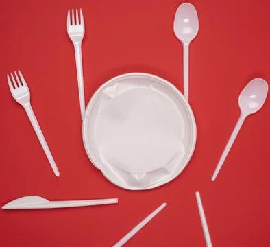 Round plate and stack of plastic forks and spoons on red background Stock Photos