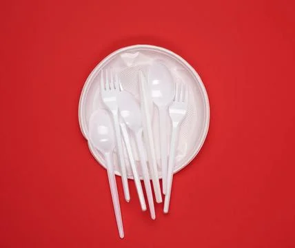 Round plate and stack of plastic forks and spoons on red background round ... Stockfoto's