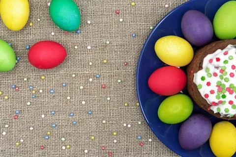 Round plate with multicolored Easter eggs and Easter cake on a burlap background Stock Photos