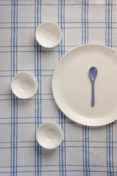 Round plate with a spoon and empty round cups on checkered tablecloths Foto stock