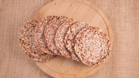 Round puffed grain crackers stacked on wooden board, light motion. Stock-Footage 332892720