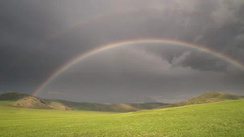Round rainbow arcs across empty grassland under dramatic storm - Ecotourism Stock Footage 339826160