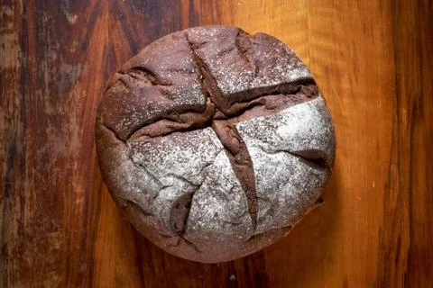 Round rye bread with molasses on the old mahogany table. Home baked bread. Stock Photos