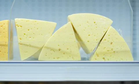 Round sectors and square cheese pieces on shelves in supermarket Stock Photos