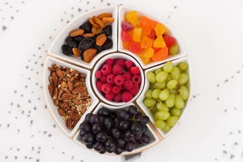 Round set of plates full of nuts, raspberries, sweets, grapes and dry fruit. Stock Photos