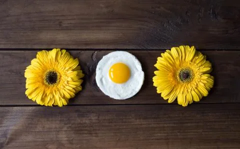 Round shaped fried egg with two yellow gerberas on dark wooden backgrond Stock Photos
