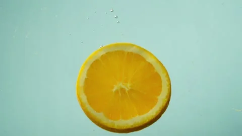 A round slice of an orange falls into the water on a blue background. Stock Footage 256911418