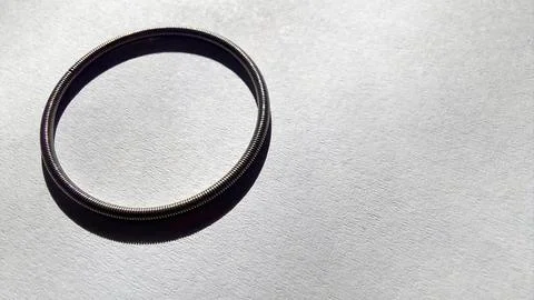 Round spring resting on smooth paper surface with gentle light casting shadow Stock Photos