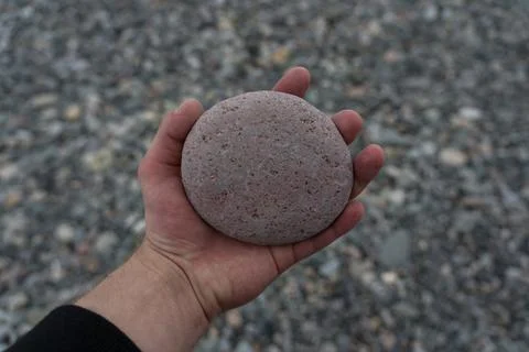 Round stone in the hand of a man on the background of the stone beach of Batu Stock Photos