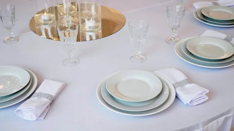 Round table with a white tablecloth served plates wine glasses and napkins Stock Footage 97716971