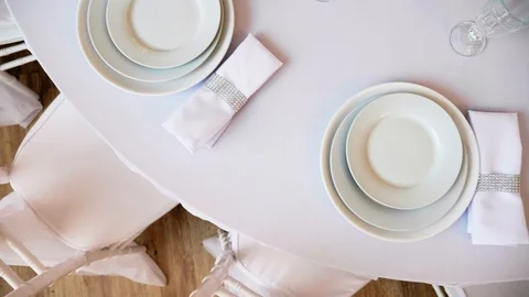 Round table with a white tablecloth served plates wine glasses and napkins Stock Footage 97717127
