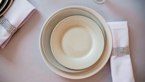 Round table with a white tablecloth served plates wine glasses and napkins Stock Footage 97717213