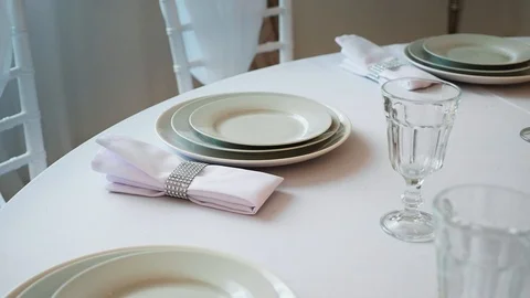 Round table with a white tablecloth served plates wine glasses and napkins Stock Footage 97717297