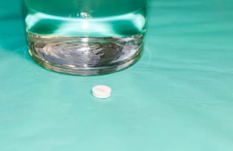 Round tablet lying on the table and next to it is a glass of drinking water. Foto stock