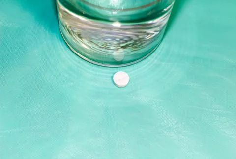 Round tablet lying on the table and next to it is a glass of drinking water. Foto stock