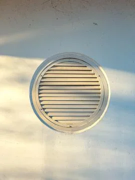 Round vent on a white wall with sunlight casting shadows in the afternoon Stock Photos