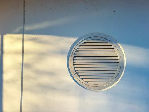 Round vent on a white wall with sunlight creating shadows in the late after.. Stock Photos
