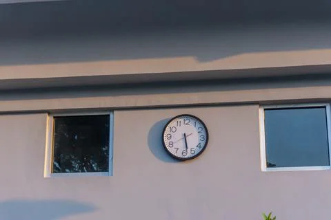 Round wall clock displayed between two square windows Stock Photos