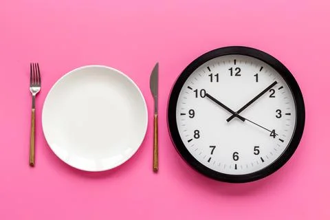 Round wall clock with empty plate. Diet or meal time concept Stock Photos