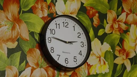 A round wall clock hangs on bright floral pattern wallpaper. Stock Footage 339100545