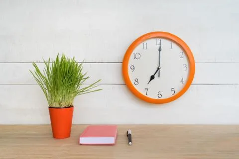 Round wall clock, pink notepad on the table and green houseplant. Workplace.  스톡 사진