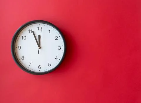 Round wall clock on red surface showing 12 o'clock, layout, top view Stock Photos