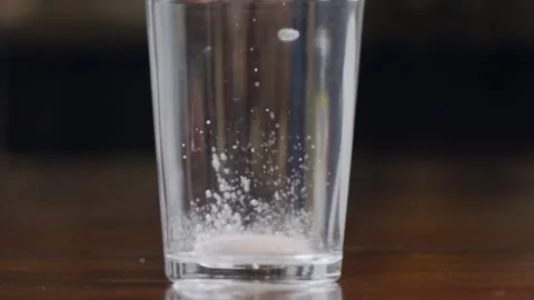 A round white effervescent pill falls into a glass of water, dissolves and Stock Footage 270237258