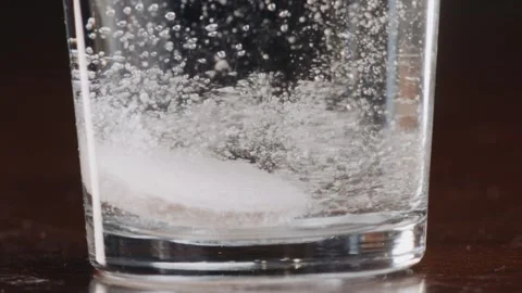 A round white effervescent pill sinks to the bottom of a glass of water Stock Footage 270237514