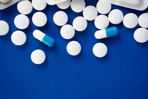 Round white tablets and capsules on blue background Stock Photos