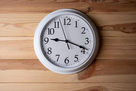 Round white wall clock hanging on a light wood background. Stock Photos