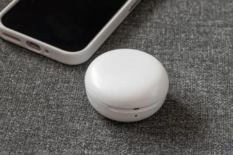Round white wireless earphone case with mobile phone on textured background Stock Photos