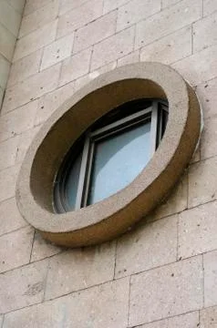 Round window with square window frame inside on facade of stone wall. Stock Photos