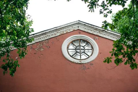 Round window under a roof in a red house facade Stock Photos