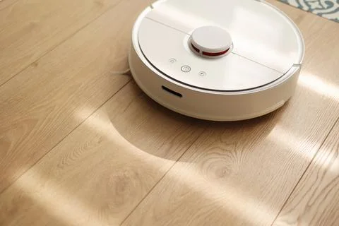Round wireless autonomous robotic vacuum cleaner on wooden floor with sunlights Stock Photos