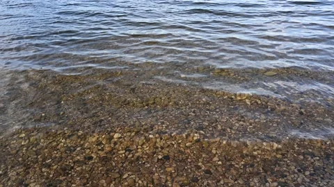 Rounded stones can be seen through clear water with small waves  Stock Footage 156145388