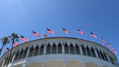 Row of American flags above white stucco pavilion with arches and palm trees Stock Footage 345369814