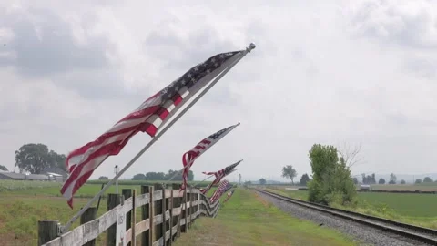 A row of American flags are flying in the wind on a train track Stock Footage 308765282