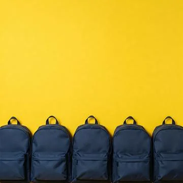 A row of backpacks on a bright yellow background with space for text Stock Photos