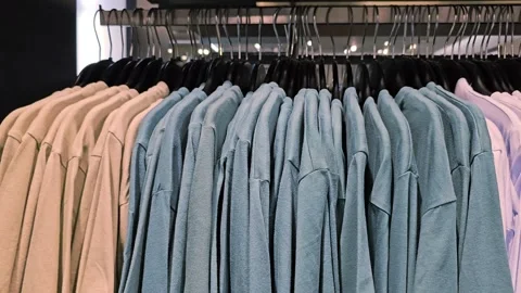 Row of beige, blue and light pink shirts hanging on black plastic hangers Stock Footage 313149123