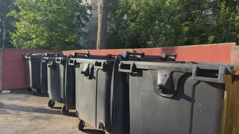 Row of black plastic trash bins with wheels near a red wall outdoors Stock Footage 341510333