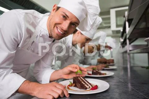 Row Of Chefs Garnishing Dessert With One Smiling At Camera