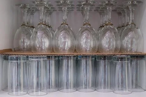 A row of clear glasses are lined up on a shelf Stock Photos