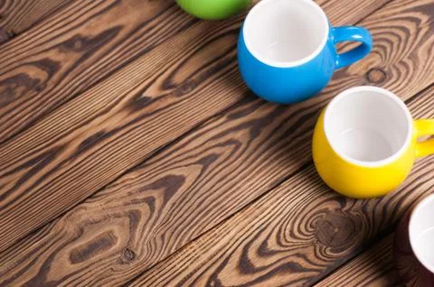 Row of colored empty ceramic clean mugs on old worn brown wooden table Stock Photos