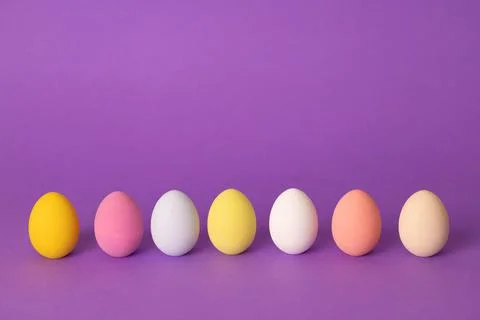 A row of colorful Easter eggs painted in simple colors on a light purple back Stock Photos