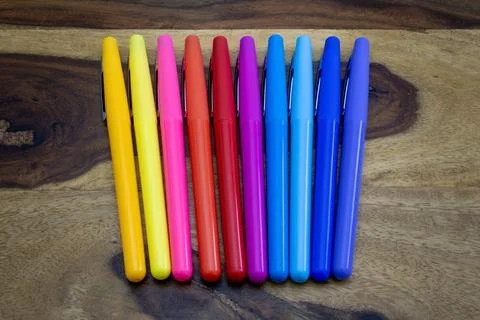 A row of colorful pens are lined up on a wooden surface Stock Photos